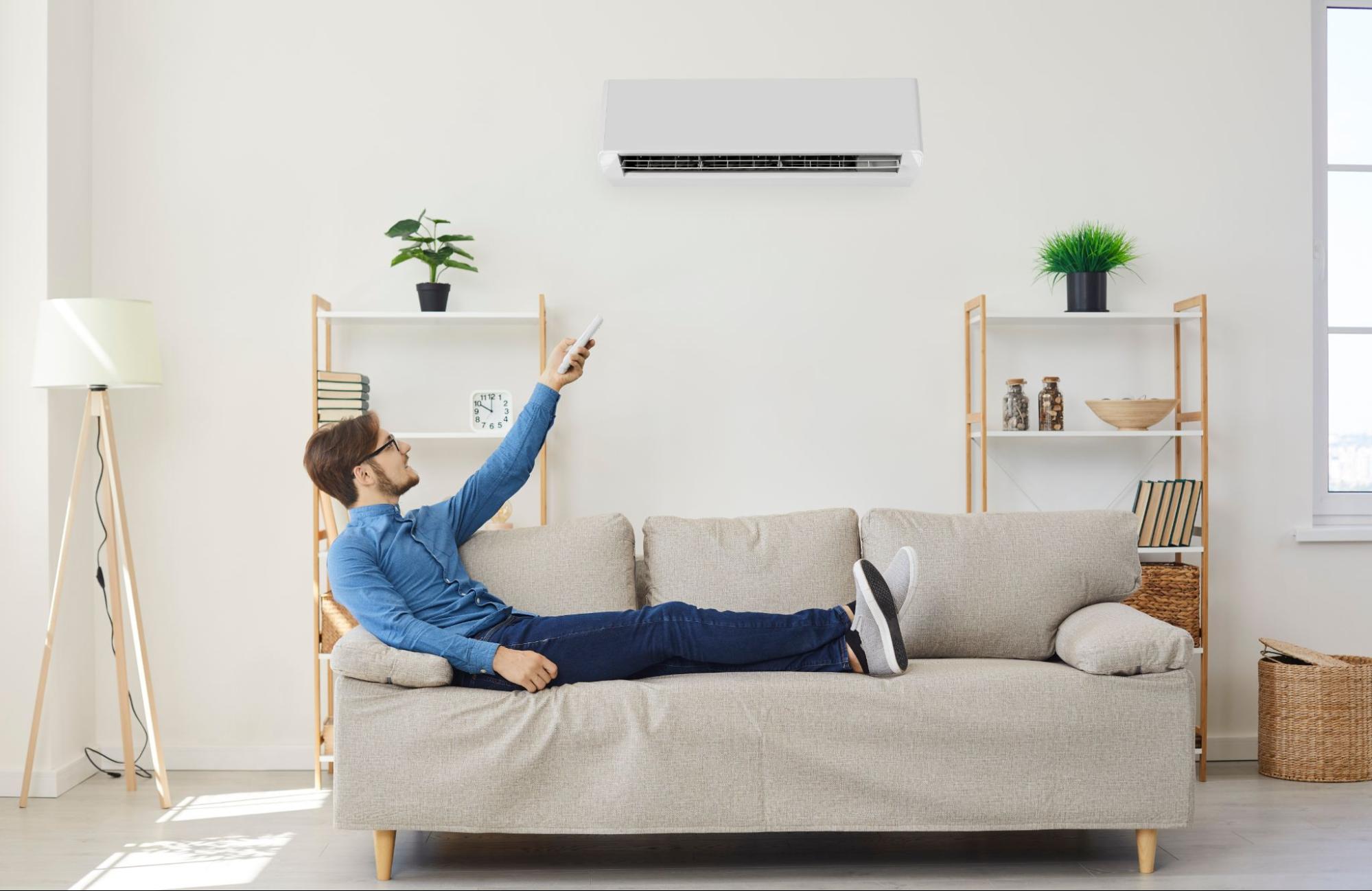 Man sitting on a couch turning on his central air conditioning with an HVAC remote